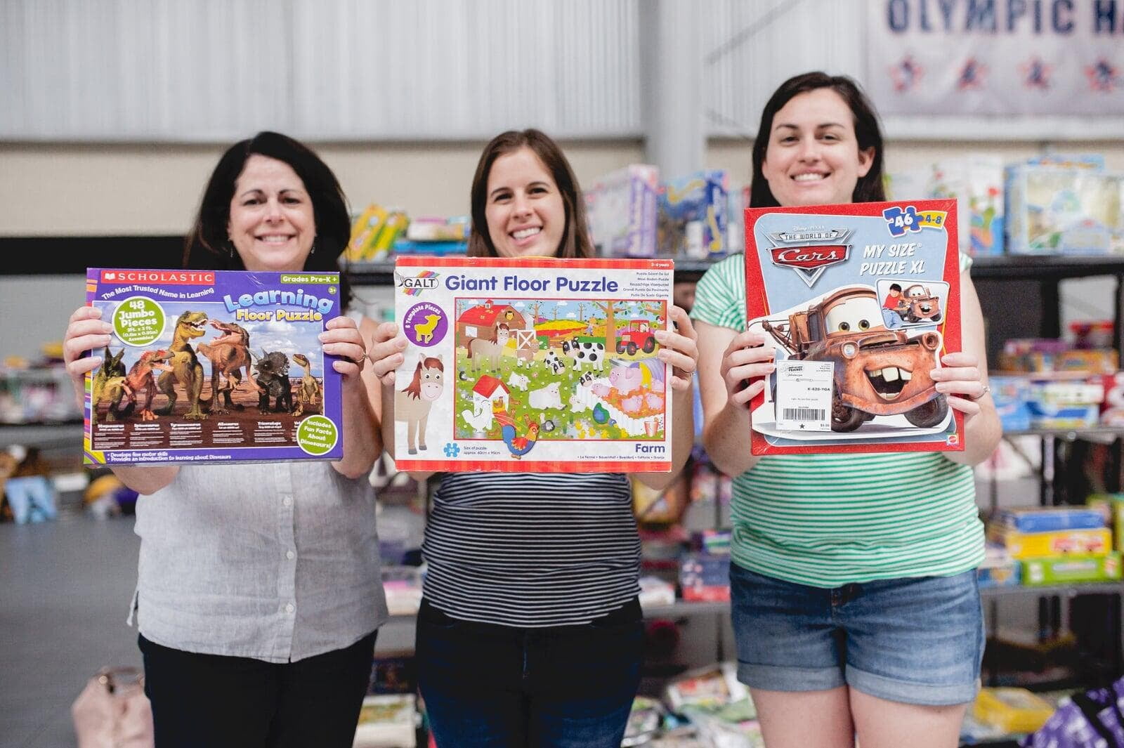 three moms holding puzzles at a JBF event